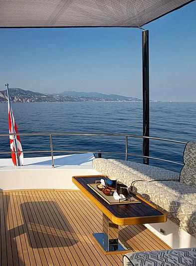 a deck with a table and chairs on it and a view of the water and mountains in the aboard A2 Yacht for Sale