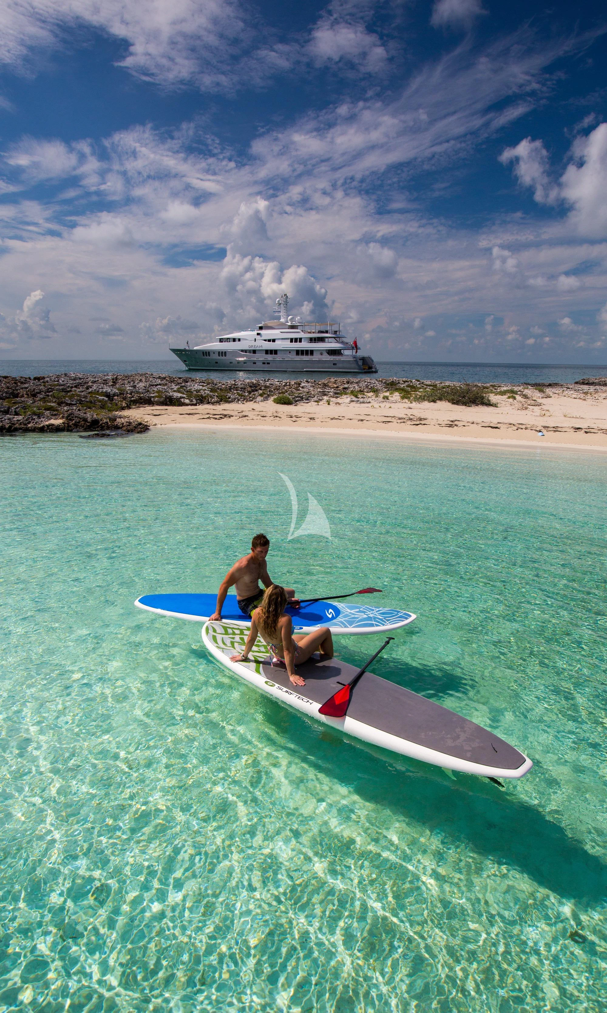 a couple of men carrying surfboards on a beach aboard DREAM Yacht for Sale
