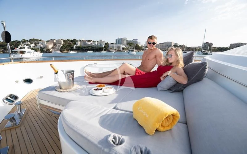 a man and woman sitting on a couch on a deck with a view of a city and water aboard CAROM Yacht for Sale