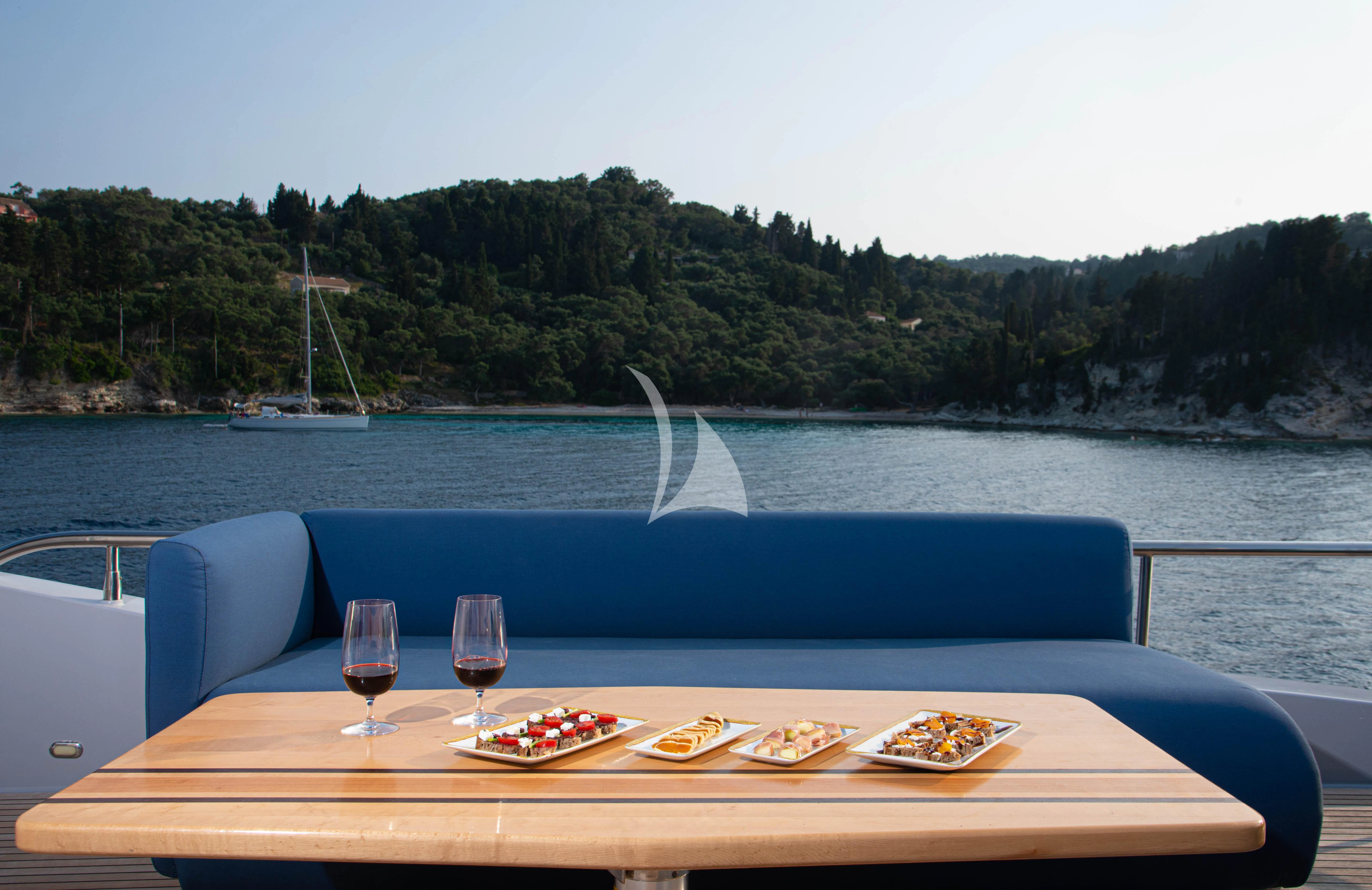 a table with food and wine by a body of water aboard STELA 117 Yacht for Sale