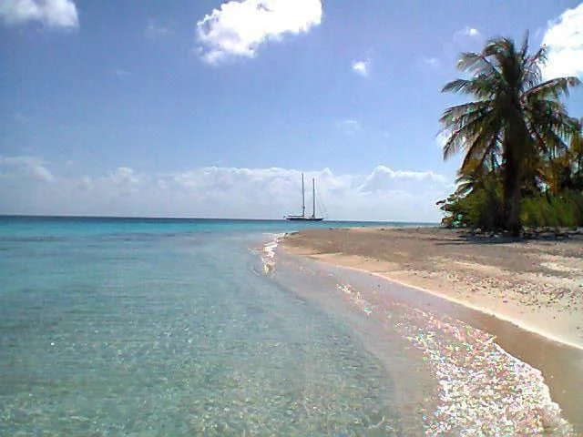 a beach with a body of water and a beach with a sailboat in the distance aboard ATHOS Yacht for Sale