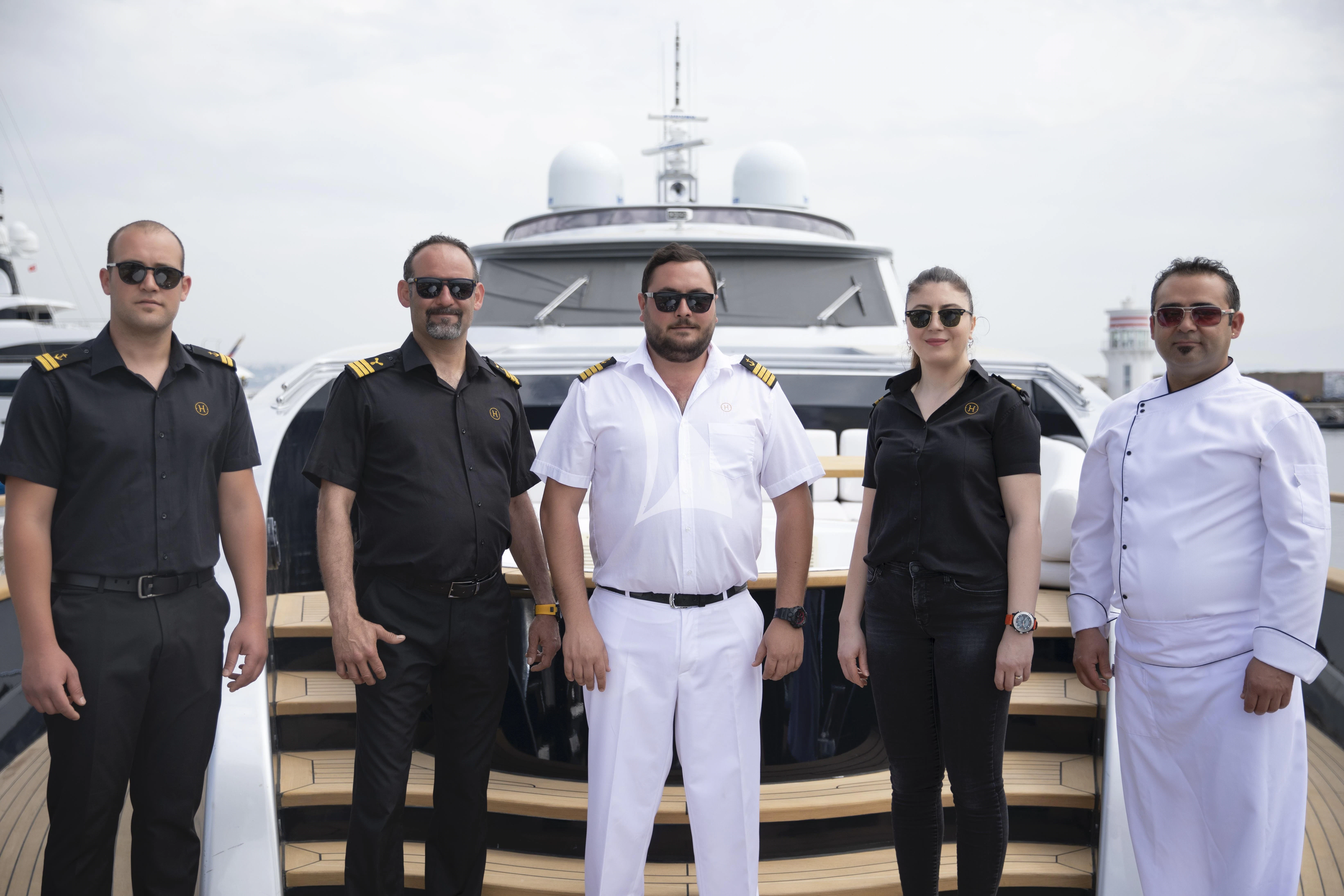 a group of men posing for a photo in front of a helicopter aboard HARUN Yacht for Charter