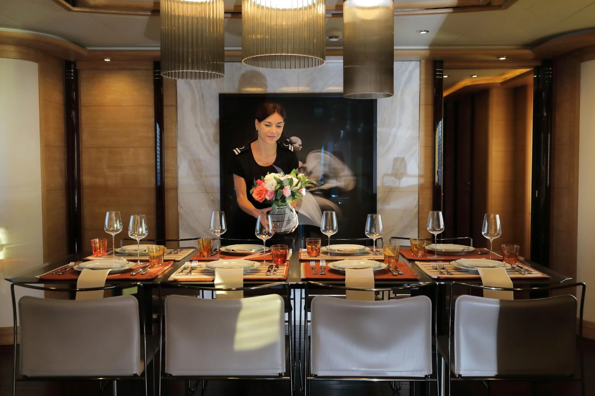 a person standing behind a table with wine glasses and flowers aboard AERO Yacht for Charter