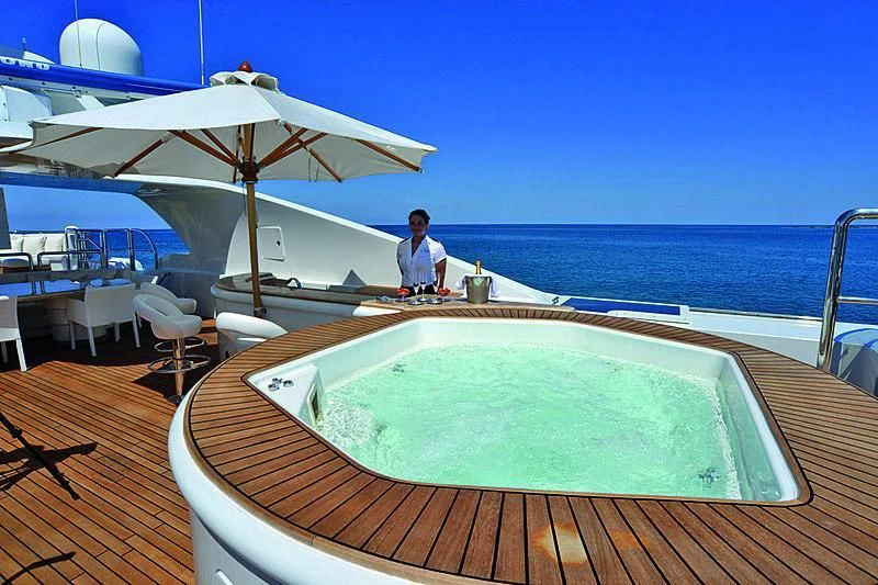 a person sitting on a deck with a pool and umbrella aboard BARENTS Yacht for Charter