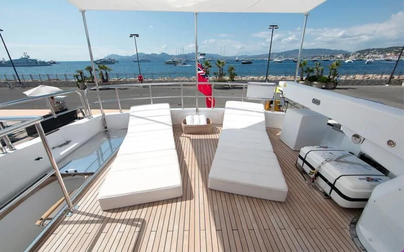 a deck with white chairs and a red and white striped flag on it aboard TUSCAN SUN Yacht for Charter