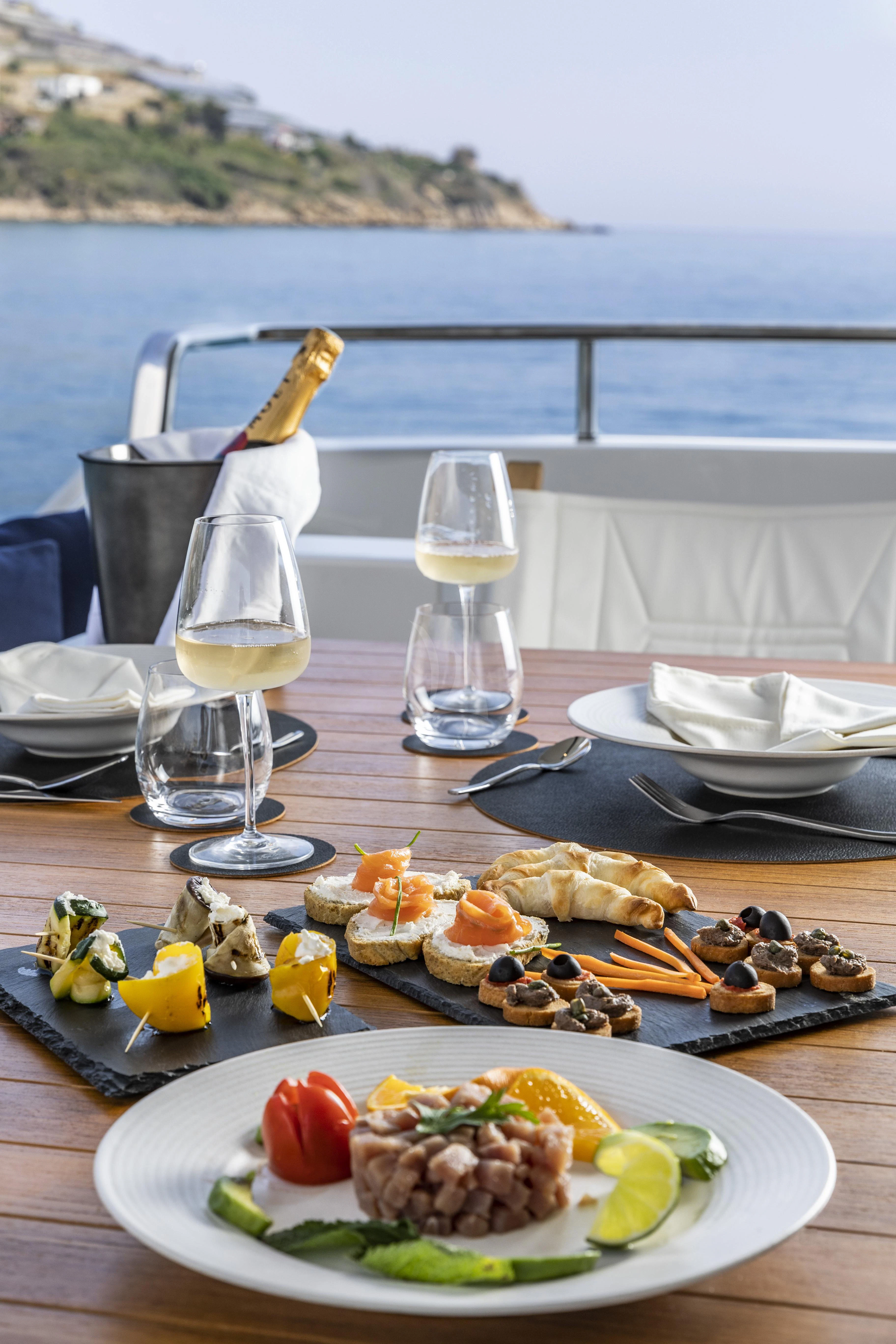 a plate of food and a glass of wine on a table aboard AMAN Yacht for Sale
