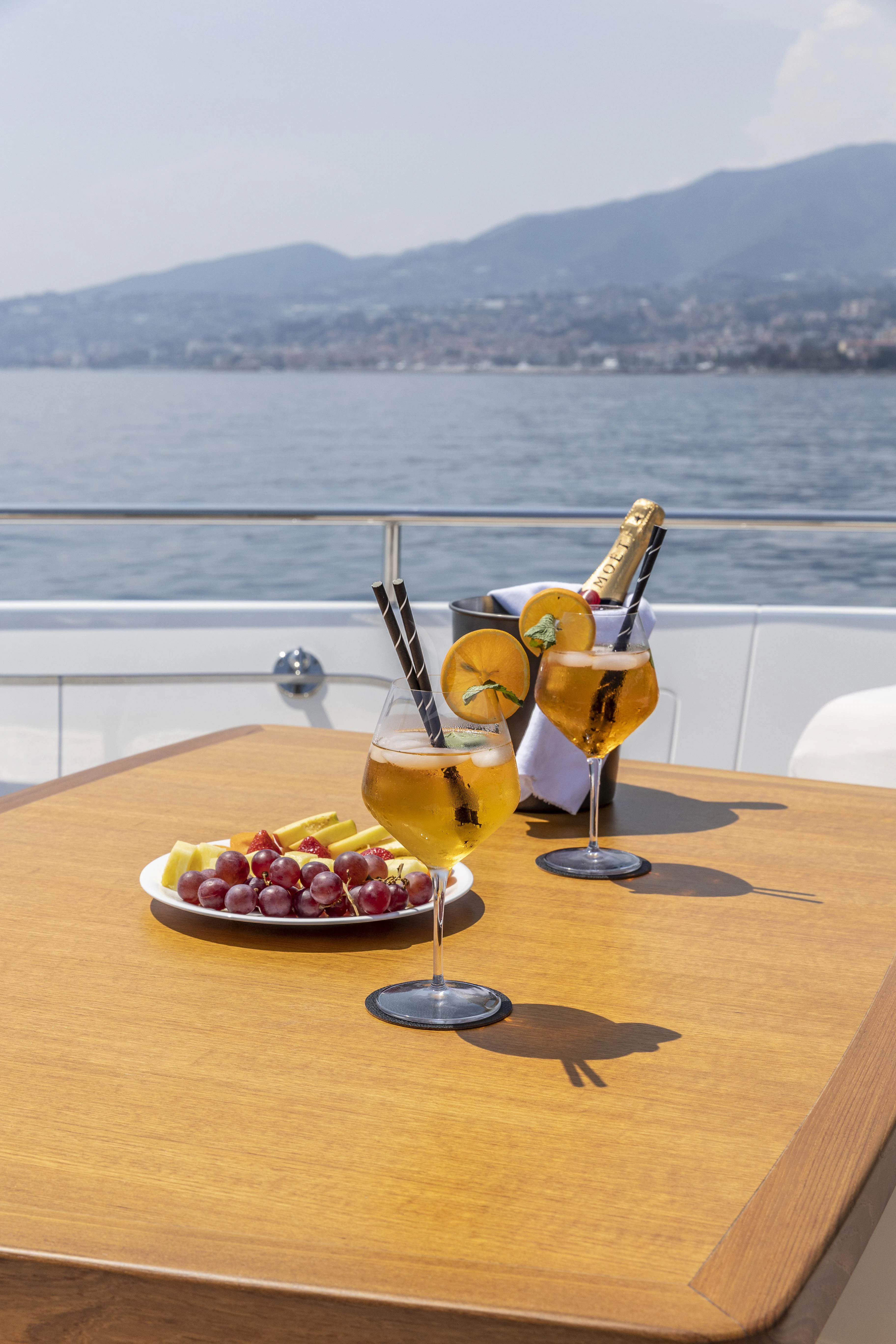 a glass of wine and a plate of fruit on a table with a view of the water and aboard AMAN Yacht for Sale