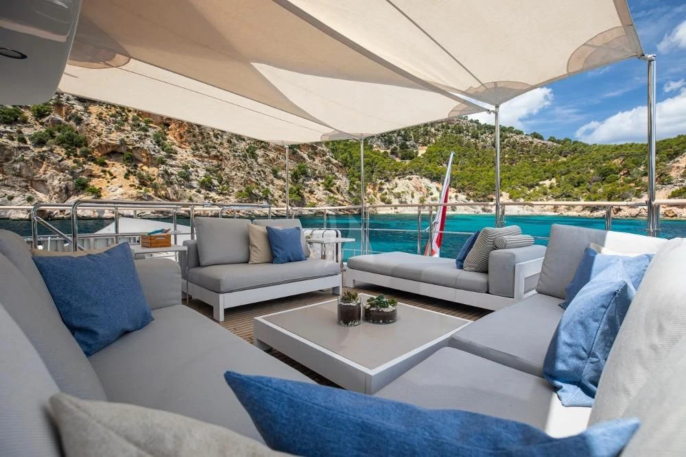a white couch and a table on a patio with a view of a mountain range aboard ORSO 3 Yacht for Sale