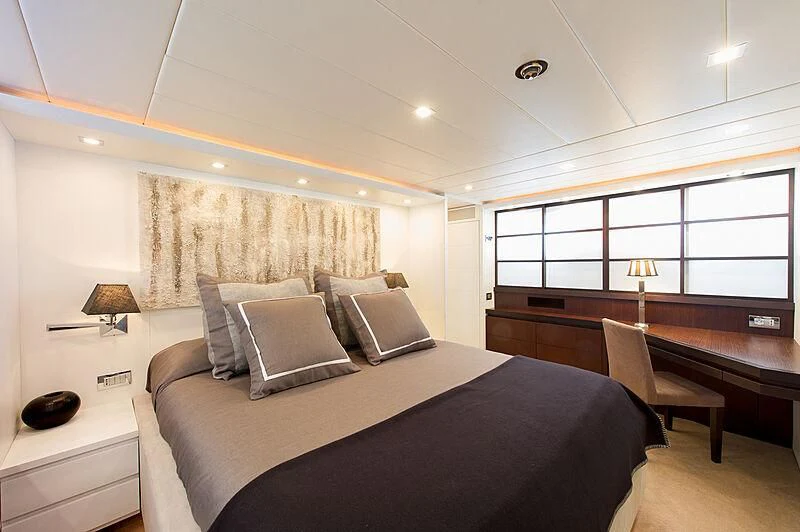 a bed with a black comforter and a desk with a window aboard LEX Yacht for Sale