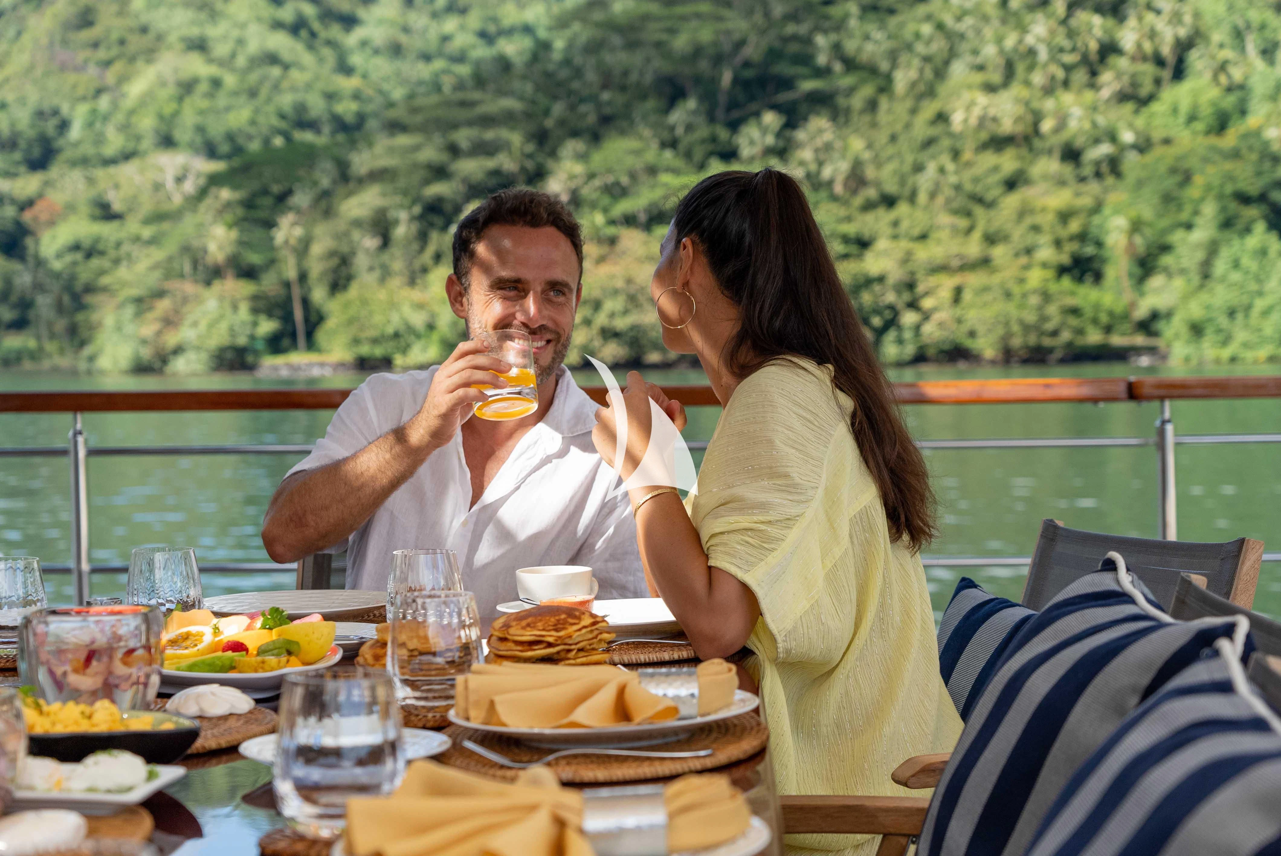 a man and woman eating at a table with a view of a forest aboard LATITUDE Yacht for Sale