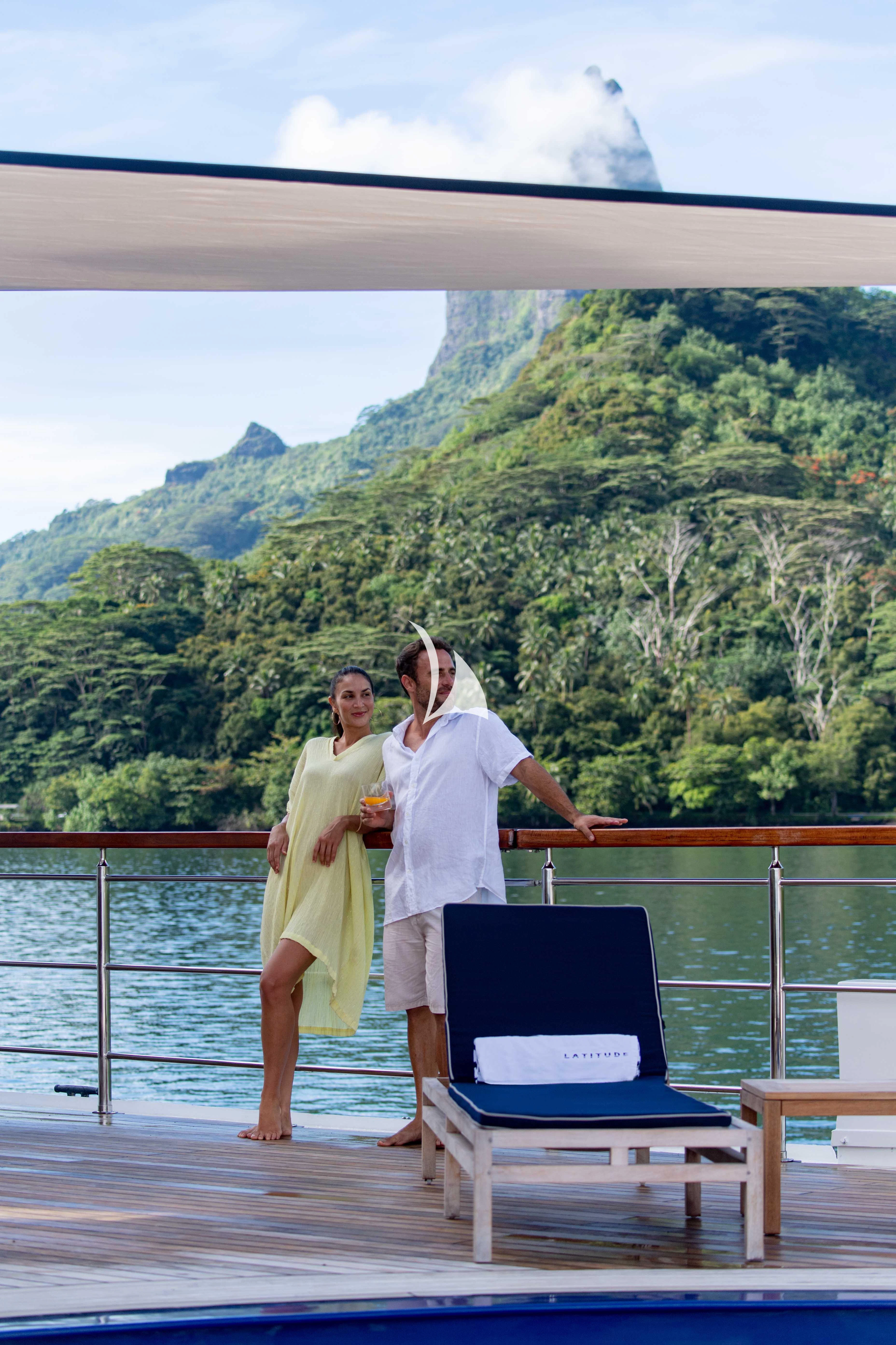 a man and woman standing on a deck with a laptop and a mountain in the background aboard LATITUDE Yacht for Sale