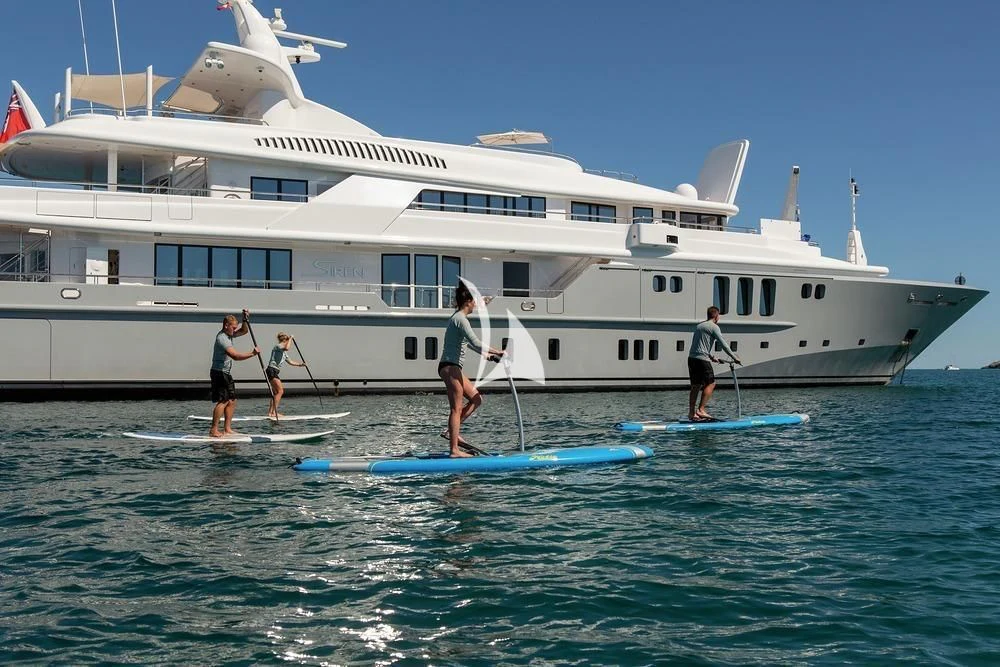 people on surfboards in front of a large white boat aboard SIREN Yacht for Sale