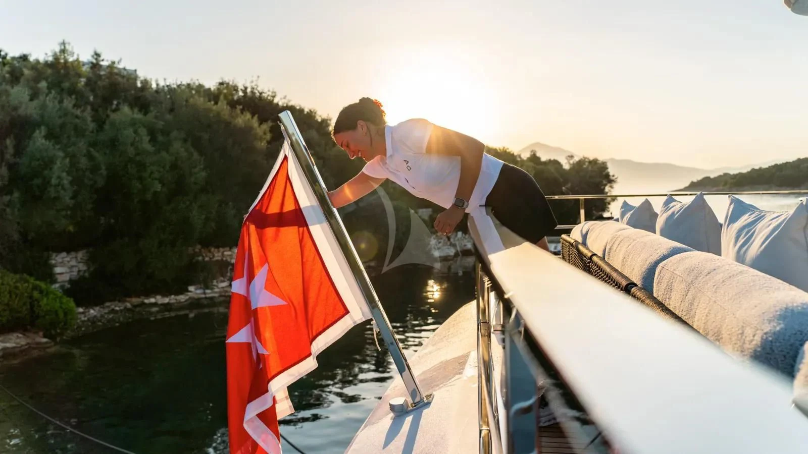 a man in a white shirt on a boat with a flag aboard AT ONE Yacht for Charter