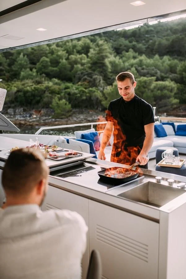 a man cooking food on a grill aboard PARALOS Yacht for Charter