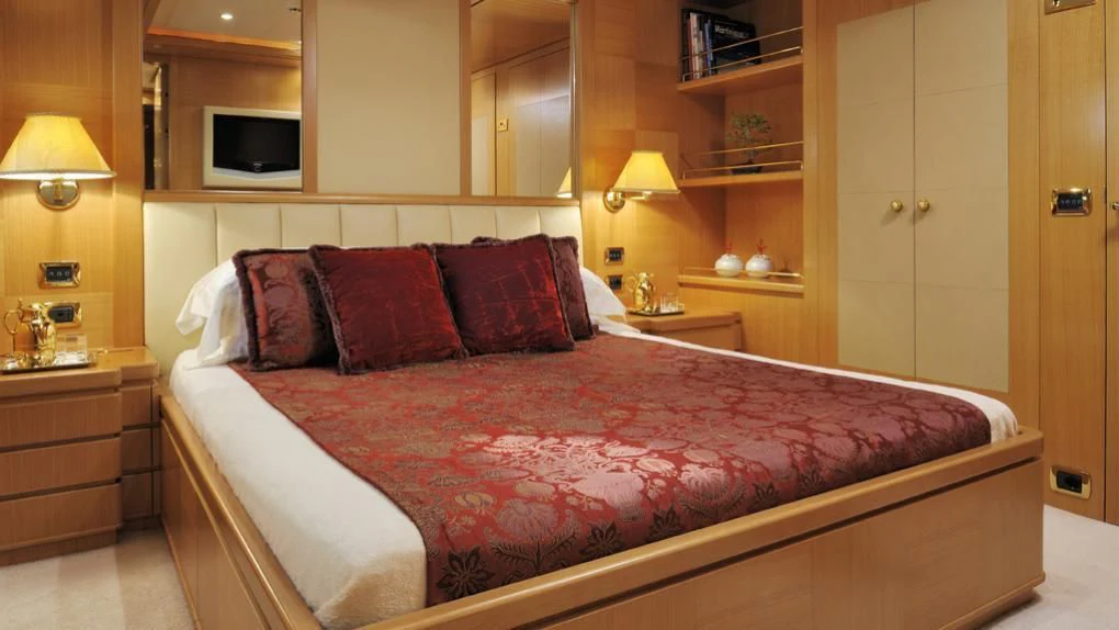 a bed with a red and white comforter and pillows aboard OASIS Yacht for Sale