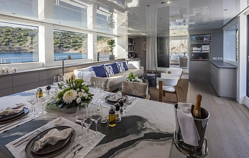 a large dining table with a large white and grey room with a blue couch and white walls aboard DINAIA Yacht for Charter