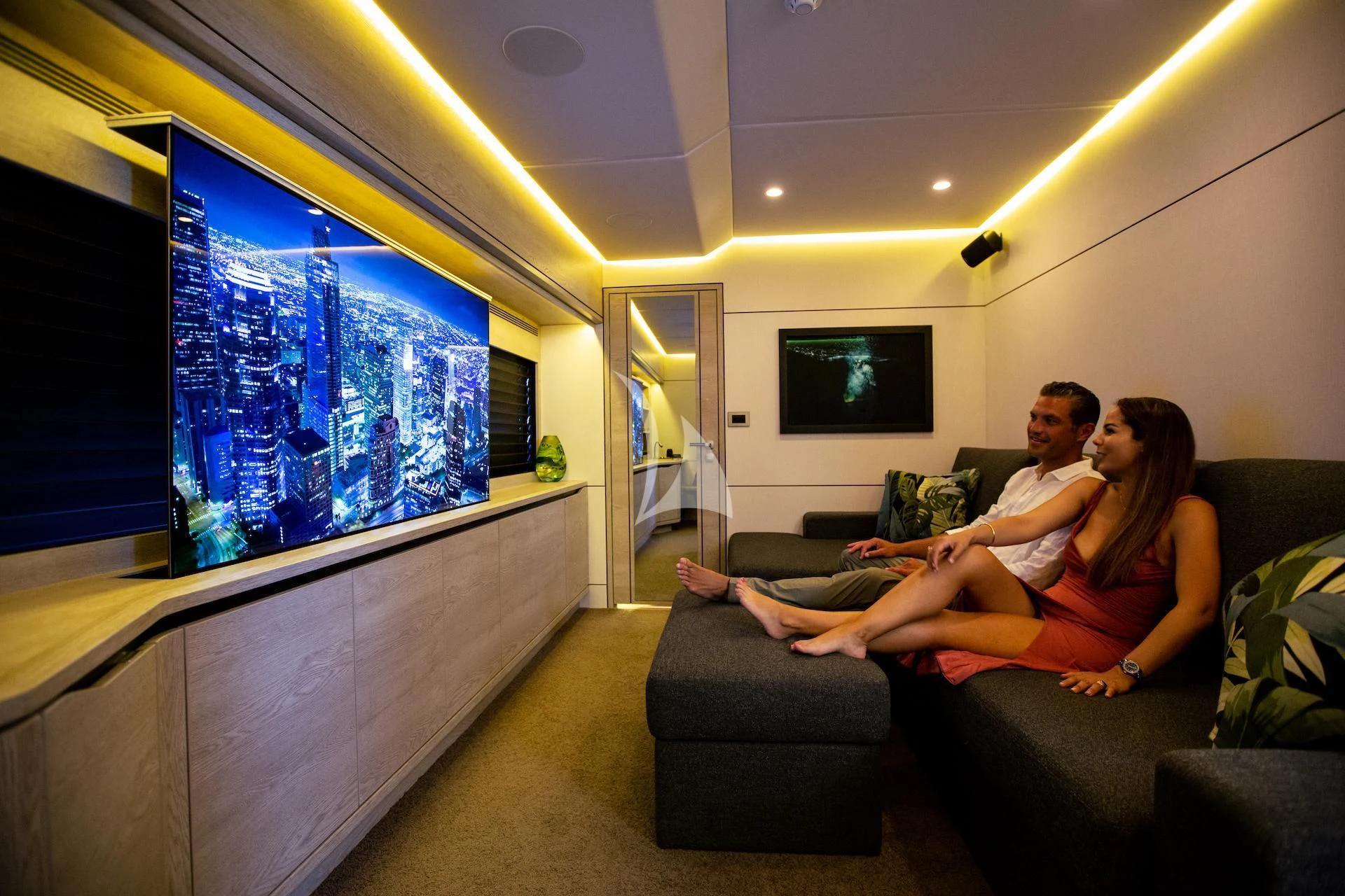 a man and woman sitting on a couch in front of a large screen aboard RUA MOANA Yacht for Sale