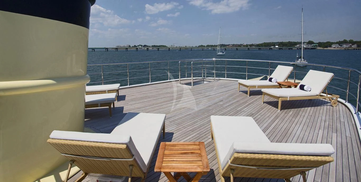 a deck with chairs and tables on it by a body of water aboard OMNIA 1 Yacht for Sale