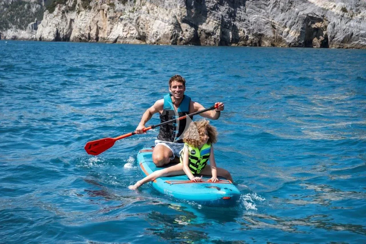 a man and a woman riding a paddle board in the water aboard AKIRA Yacht for Sale