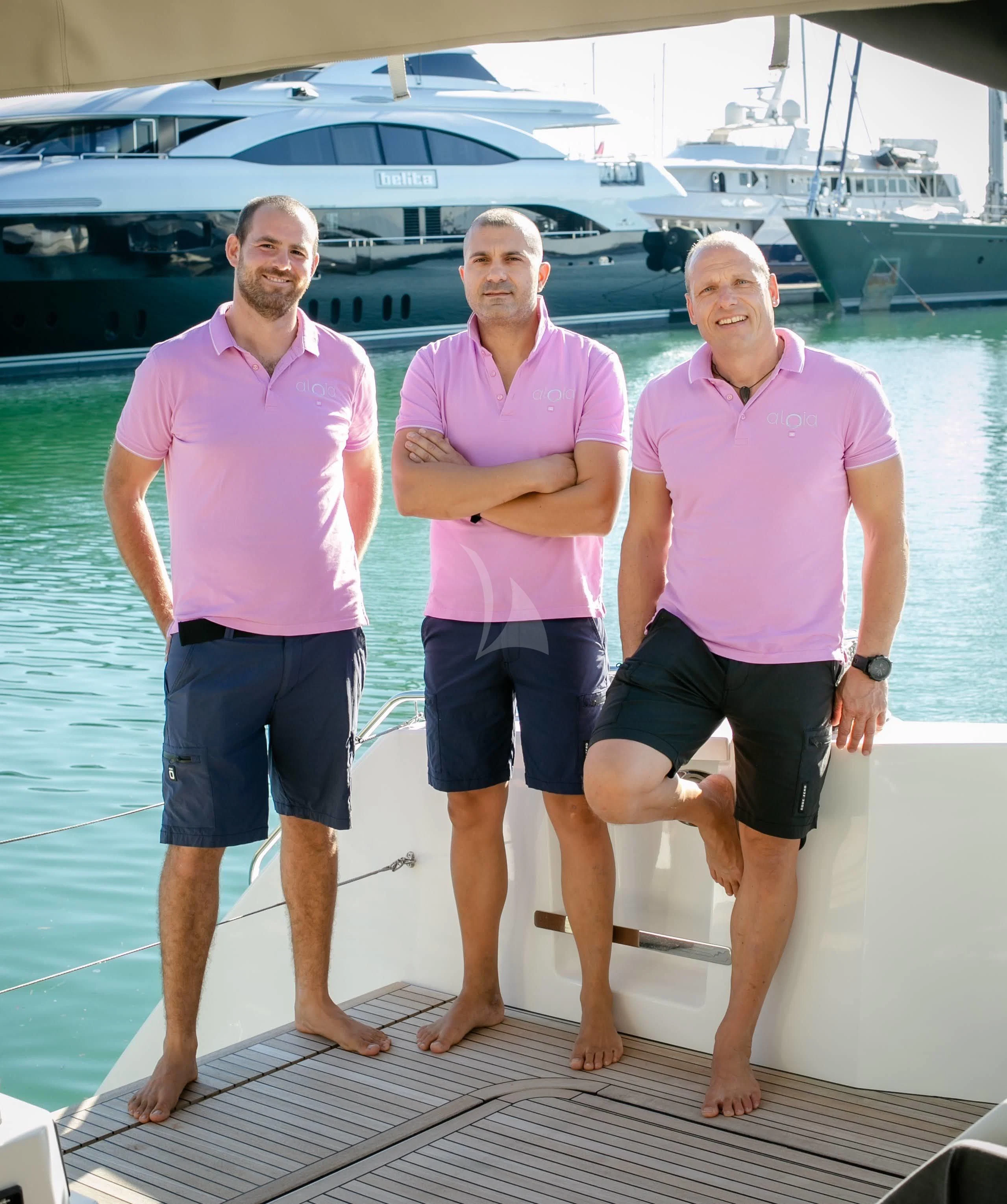 a group of men posing for a photo in front of a boat aboard ALOIA Yacht for Charter