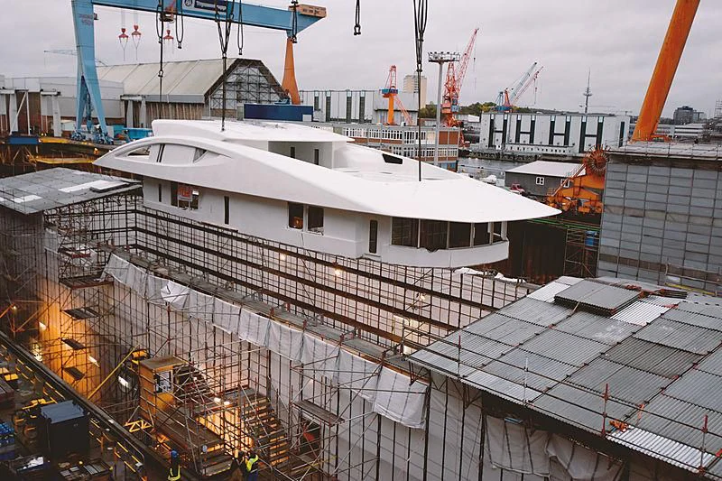 a large white building with a crane with HMS M33 in the background aboard BLACK SHARK Yacht for Sale