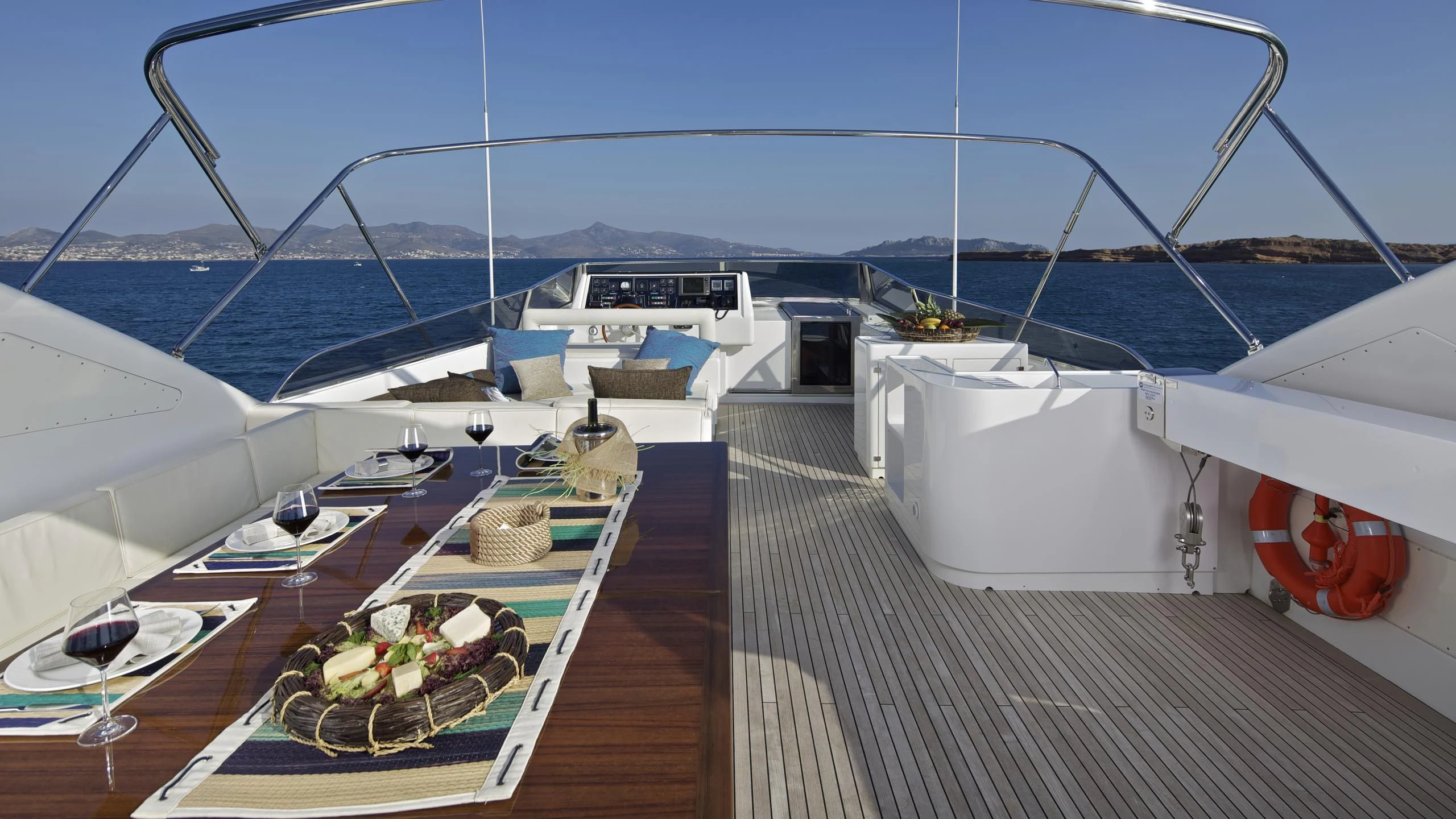 a deck with a table and chairs on it and a view of the ocean and mountains in the aboard HELIOS Yacht for Charter