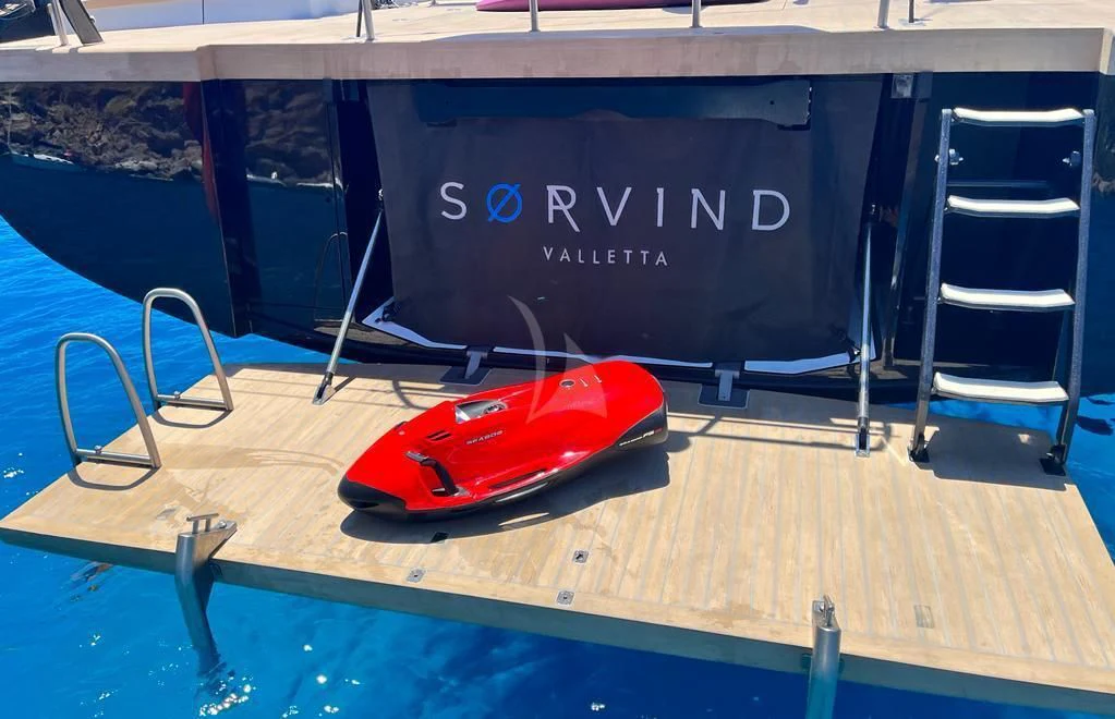 a red and black toy car on a wood surface next to a black chair and a white sign aboard SORVIND Yacht for Charter