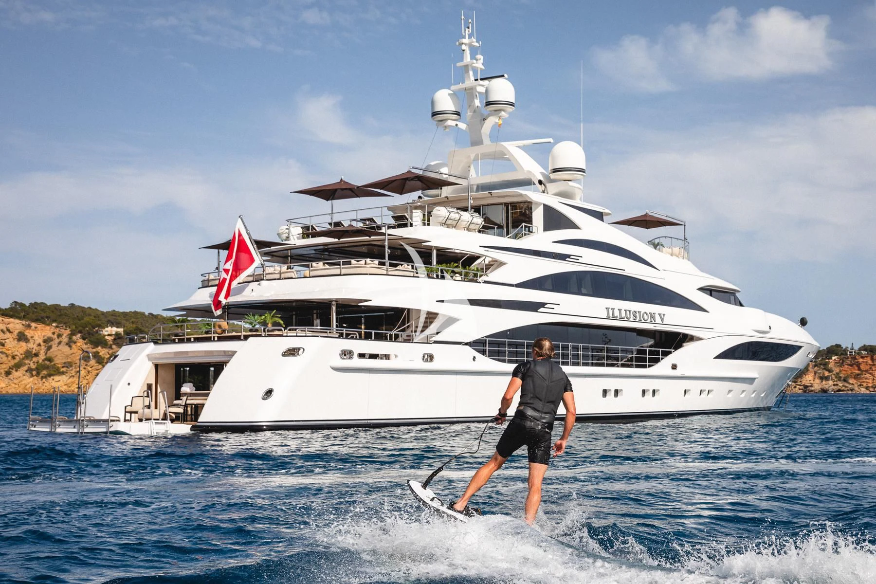 a man on a surfboard in front of a large white boat aboard ILLUSION V Yacht for Charter