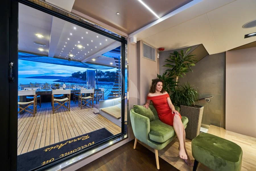 a person sitting on a couch in a room with a large window aboard RARA AVIS Yacht for Charter