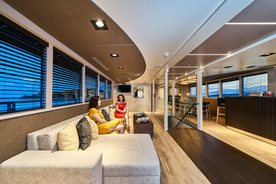 a couple of people sitting on a couch in a room with a large window and a wood floor aboard RARA AVIS Yacht for Charter