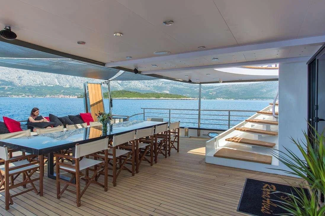 a person sitting at a table in a restaurant with a body of water in the background aboard RARA AVIS Yacht for Charter