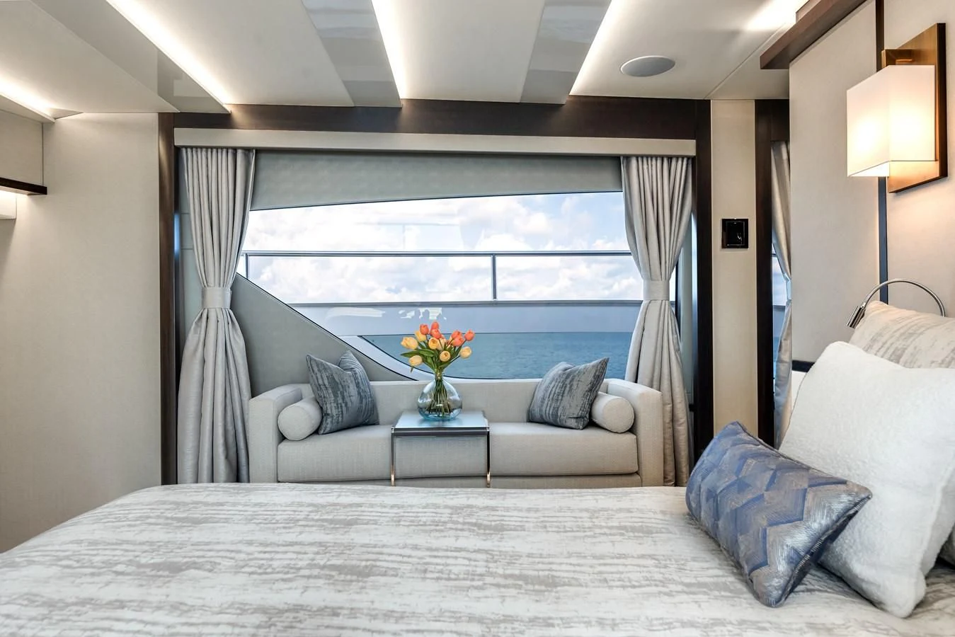 a large white bed with pillows and a table with a vase of flowers on it aboard TRIGGER HAPPY Yacht for Sale
