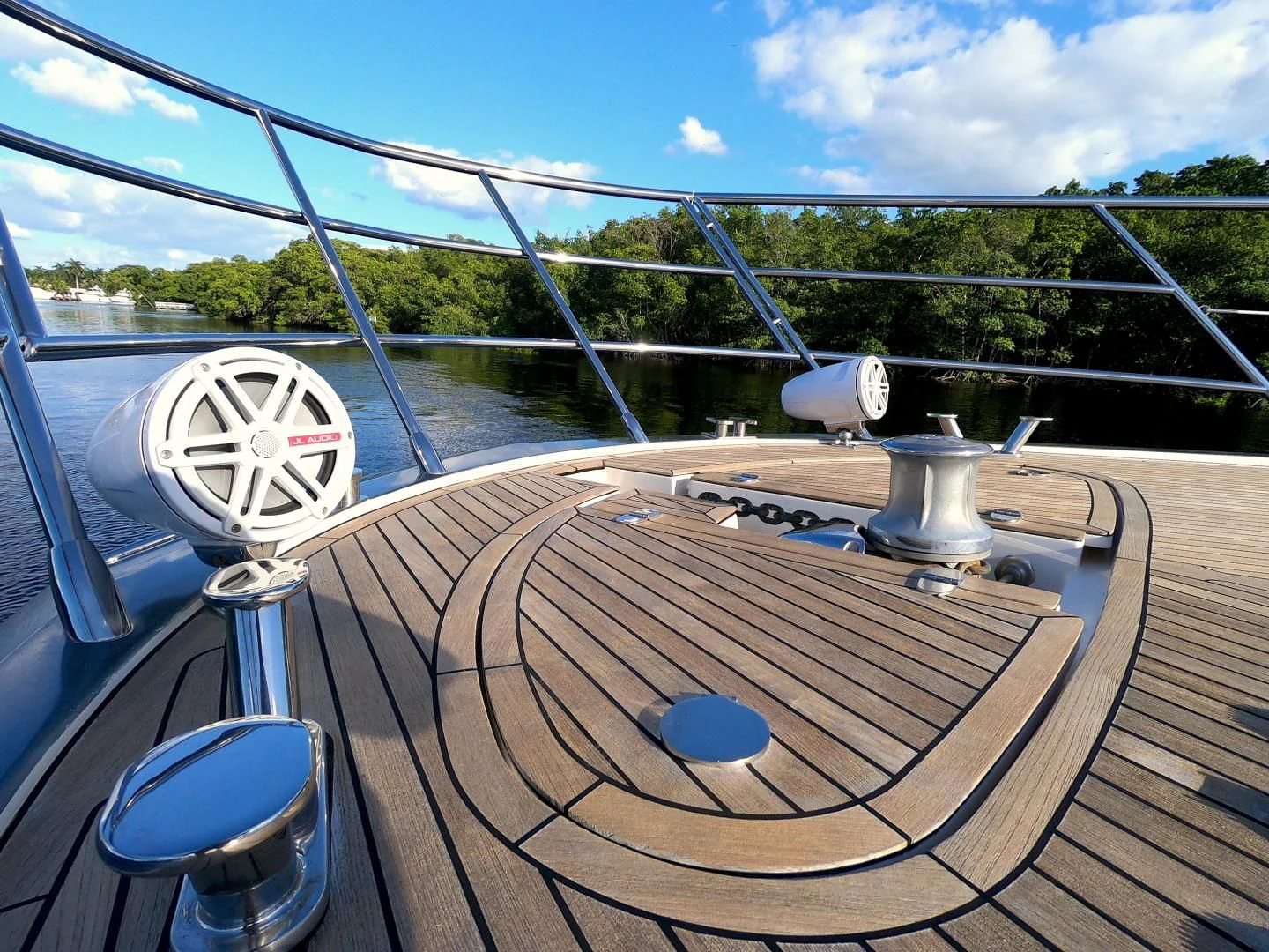 a wooden deck with a round table and a metal railing with trees and blue sky aboard BT 2 Yacht for Sale