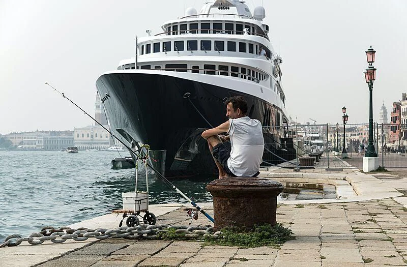 a man sitting on a dock with a large boat in the background aboard FREEDOM Yacht for Sale