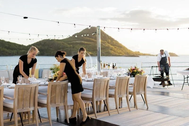 a group of women sitting at a table on a deck with a body of water in the background aboard NAIA Yacht for Sale