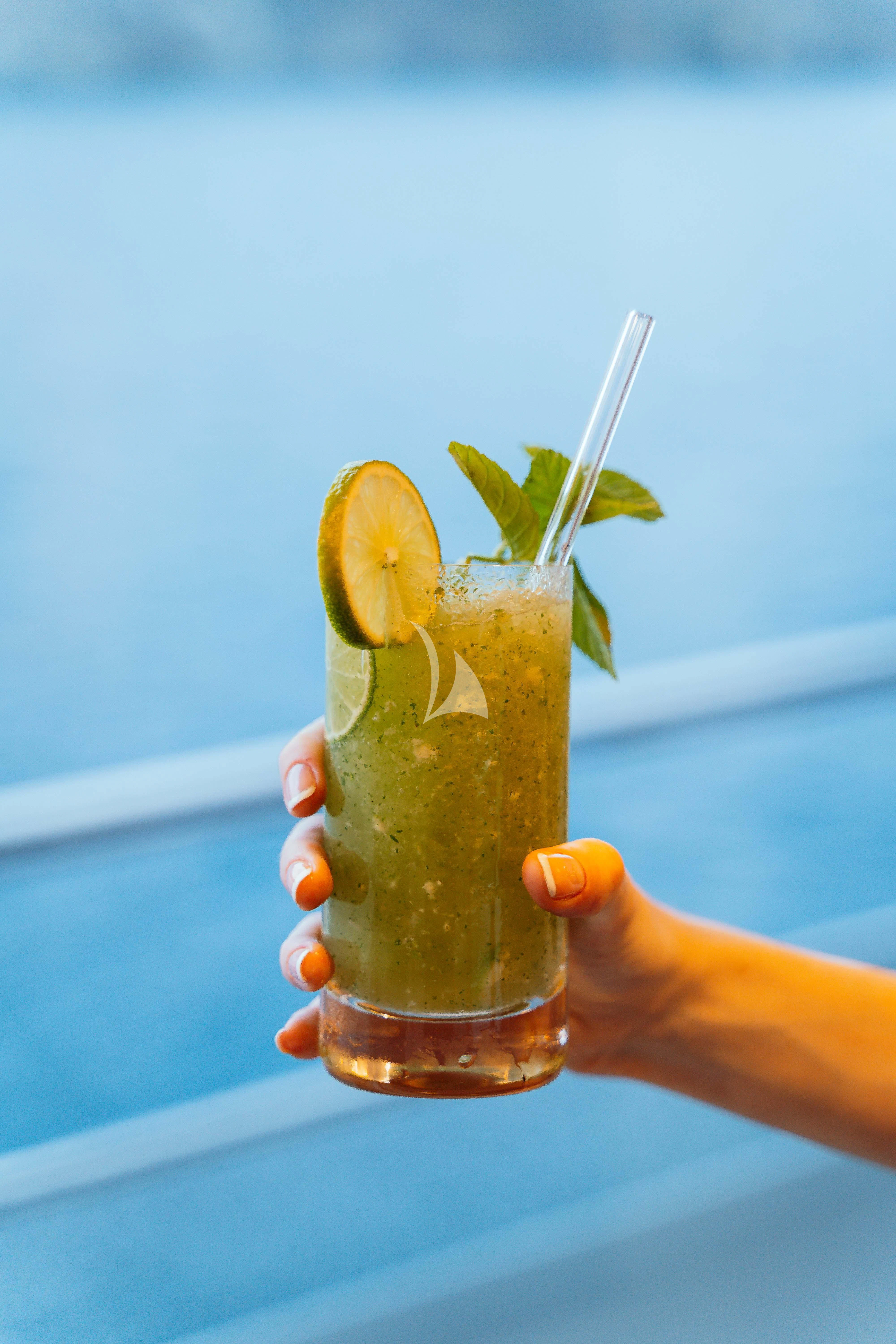 a hand holding a drink with a straw and a lime slice aboard HEEUS Yacht for Sale
