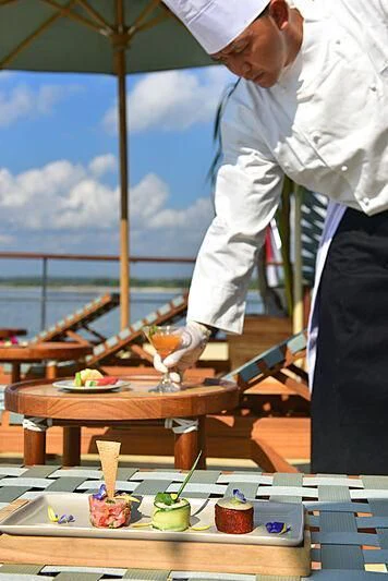 a man pouring a drink into a glass on a table aboard KUDANIL EXPLORER Yacht for Sale