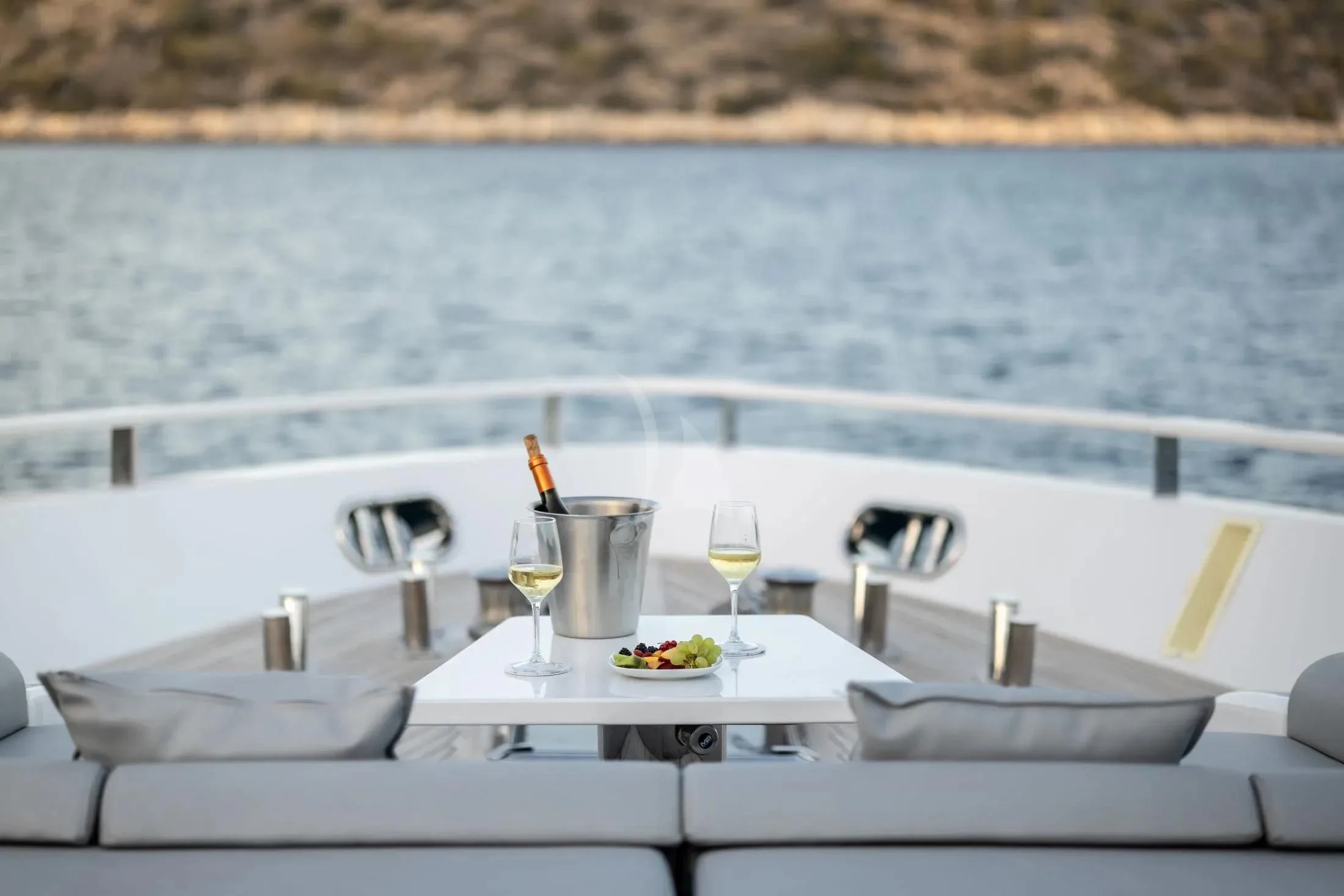 a table with a glass of wine on it and a view of the water and land in the aboard MAC Yacht for Sale