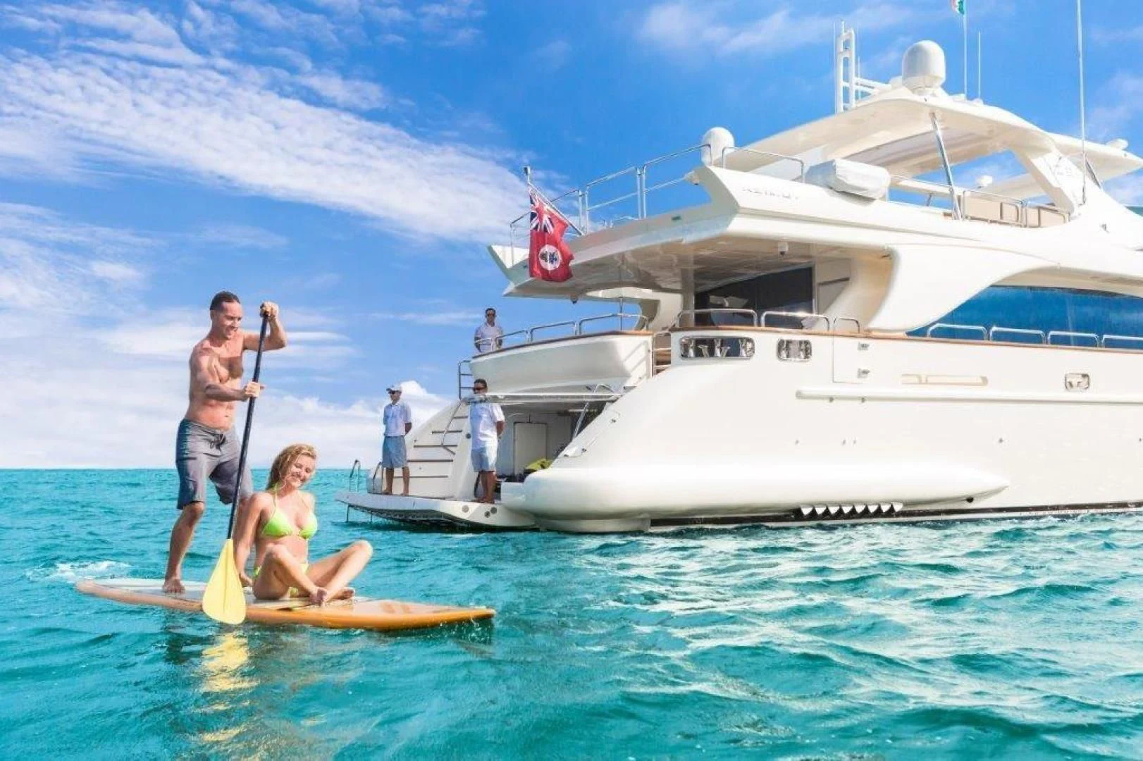 a man and woman on a paddle board in front of a white boat aboard AMANECER Yacht for Sale