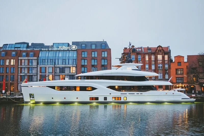a large white and yellow boat on water in front of a building aboard ACE Yacht for Sale