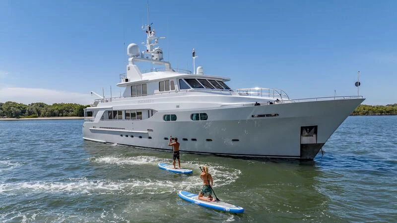 a couple of people on a surfboard in front of a large white boat aboard PLEIADES II Yacht for Sale