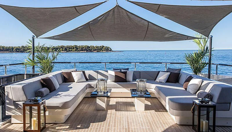 a large white couch with a table and chairs on a patio by a body of water aboard GEMS 2 Yacht for Sale