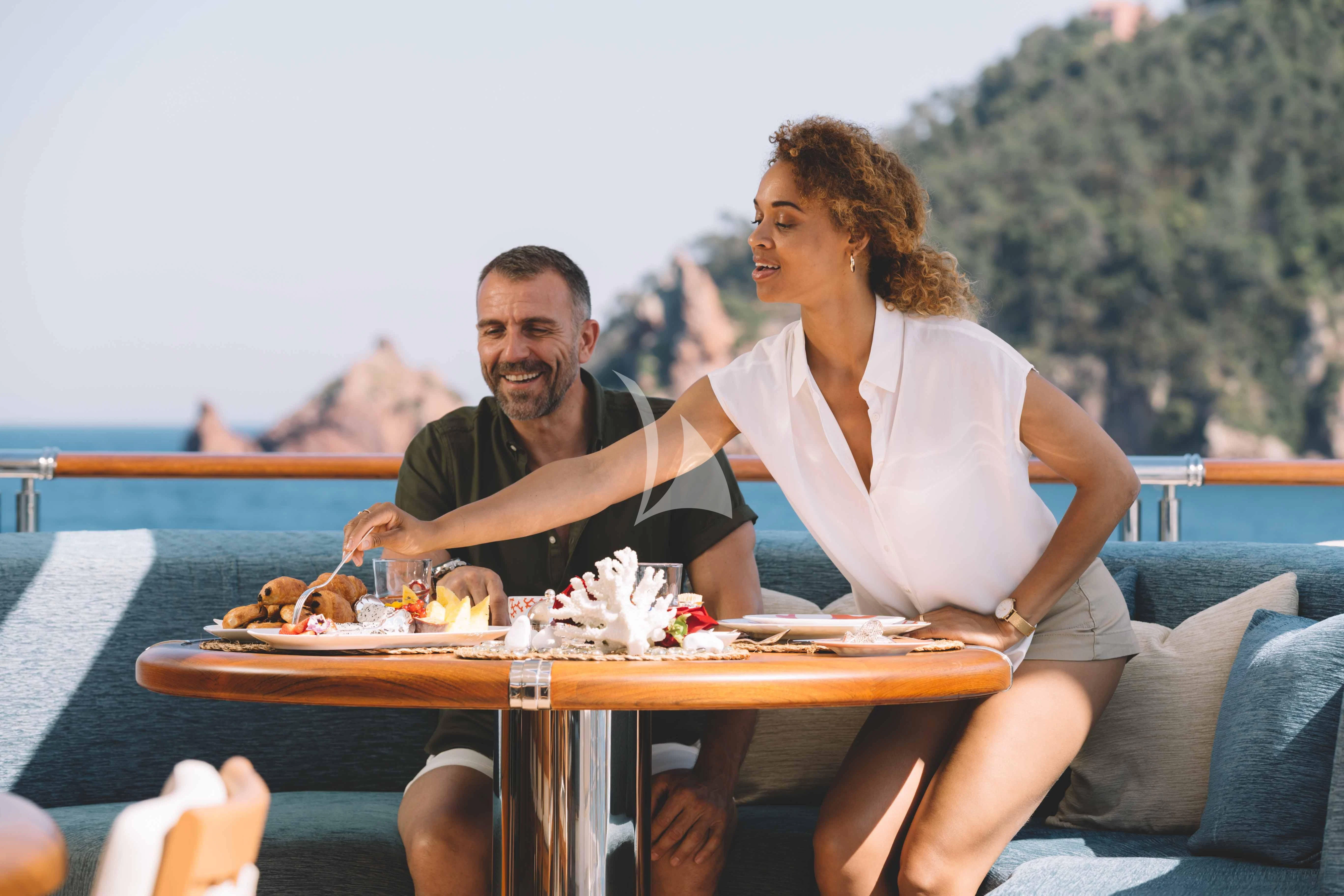 a man and a woman sitting at a table with food on it aboard WHEELS Yacht for Sale