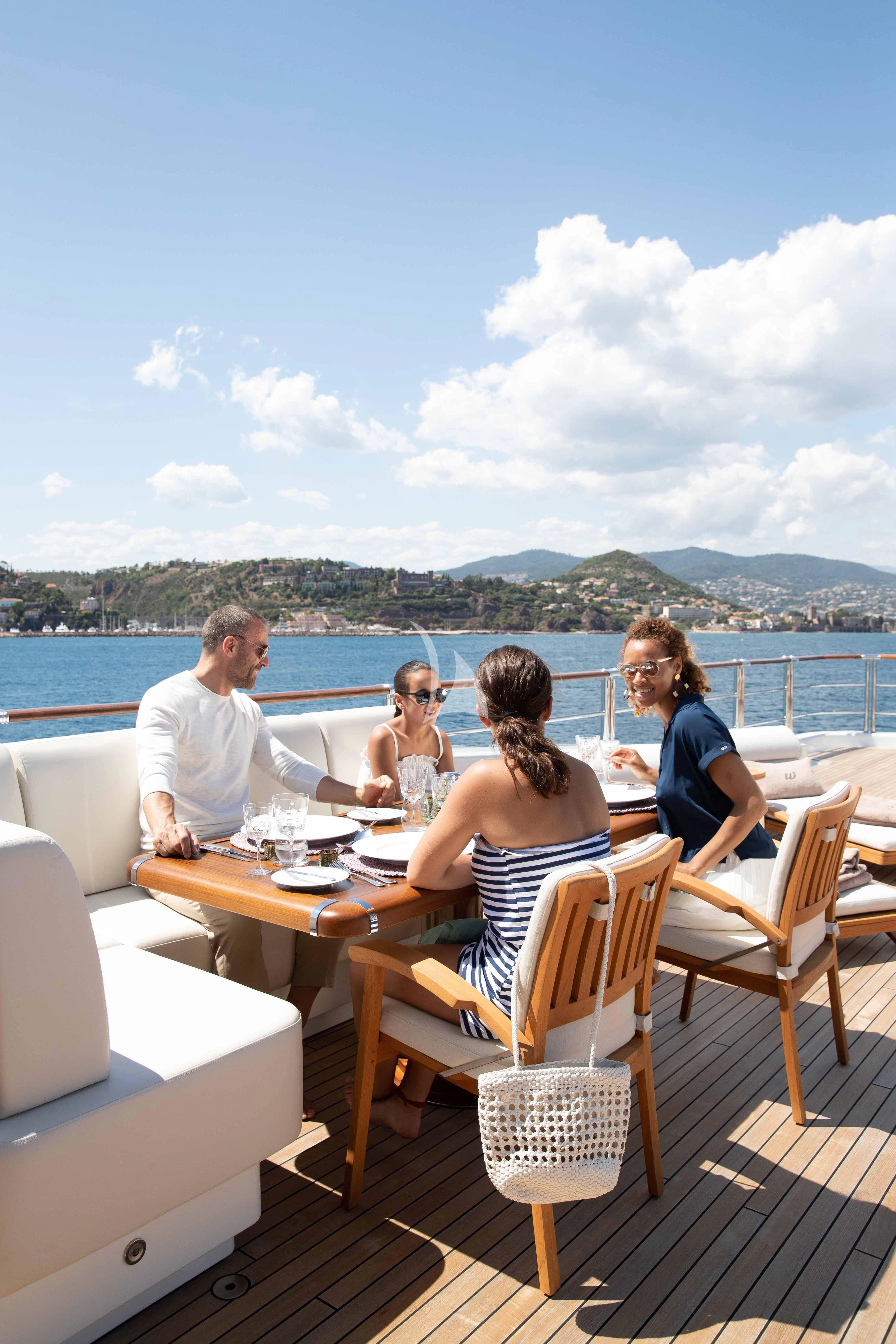 a group of people sitting around a table on a deck overlooking a body of water aboard WHEELS Yacht for Sale