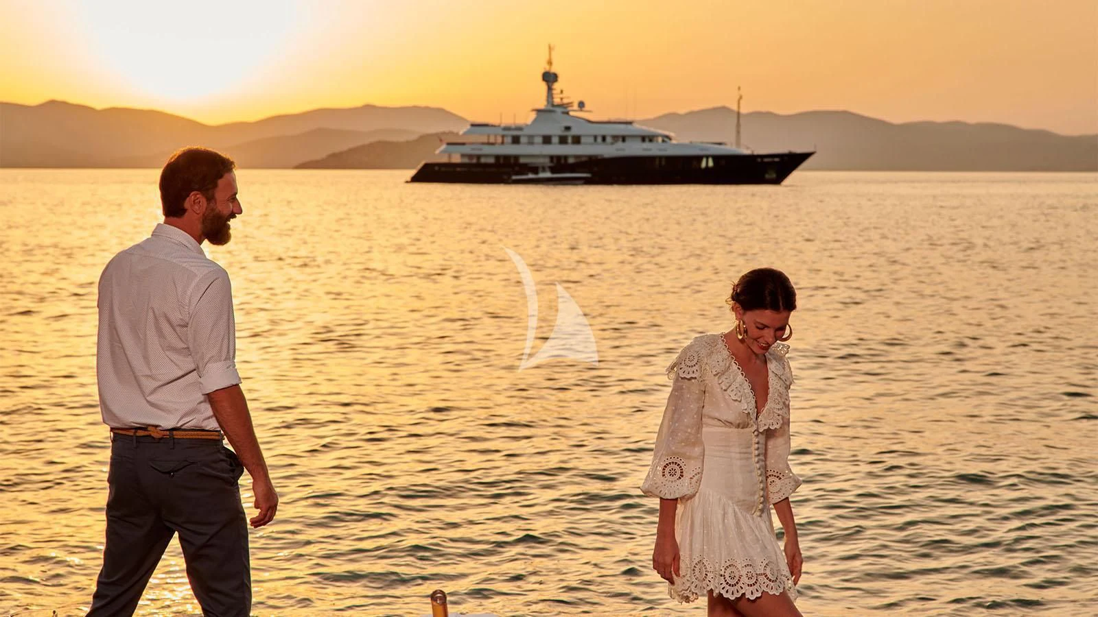 a man and woman walking on a beach with a boat in the background aboard RARE FIND Yacht for Charter