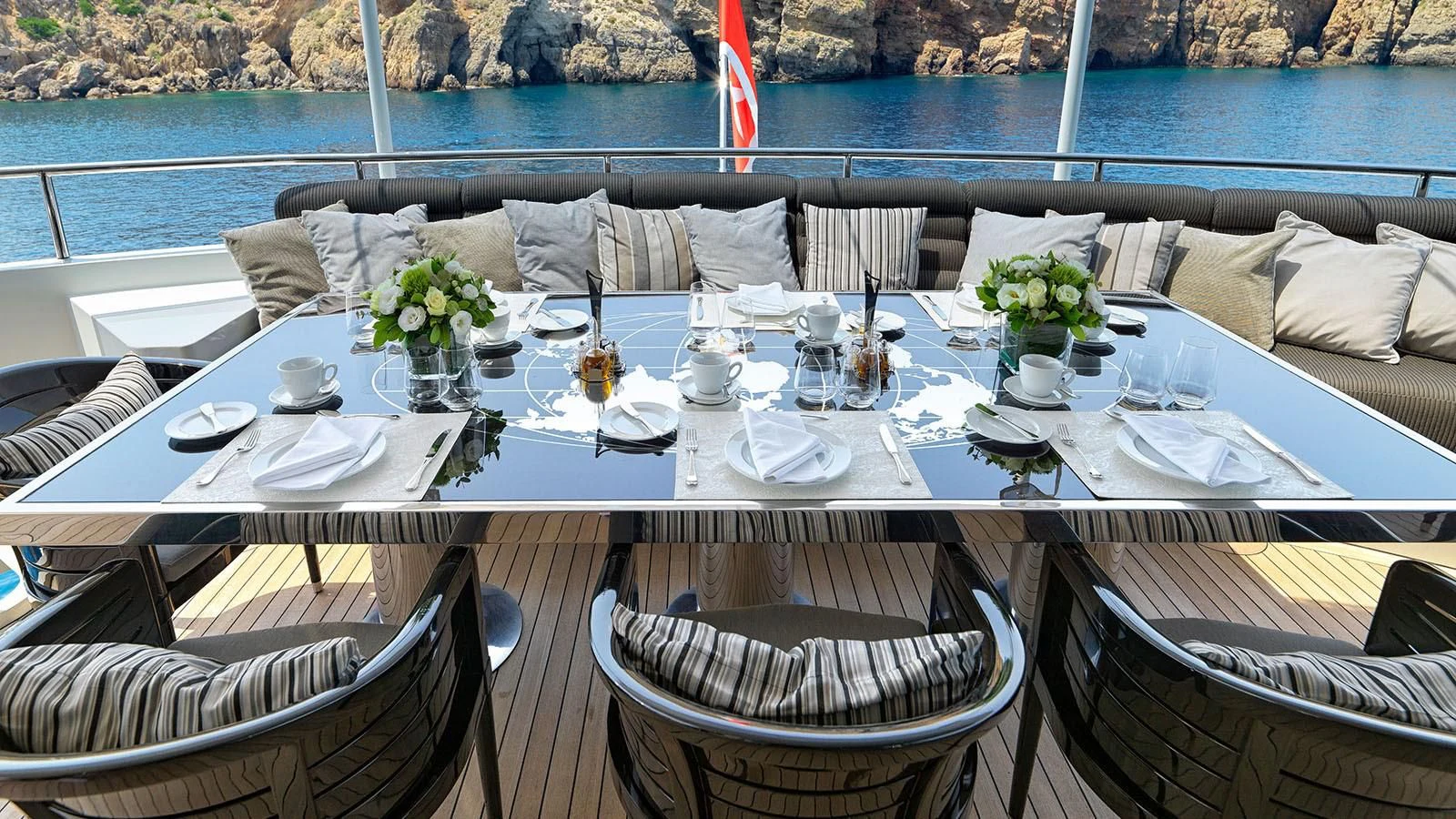 a table set with a white cloth and chairs with a body of water in the background aboard BLISS Yacht for Sale