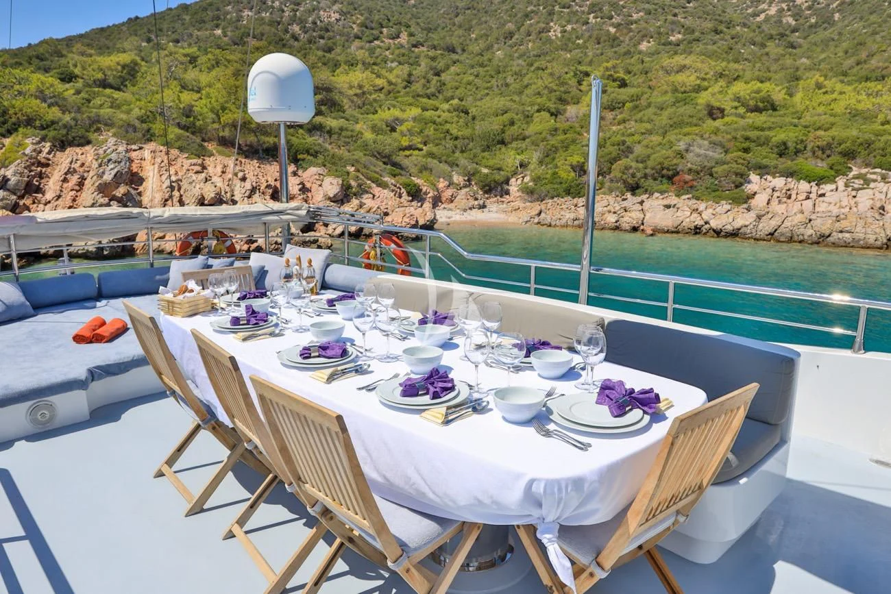 a table set for a meal on a patio with a large hill in the background aboard CANARIA Yacht for Sale