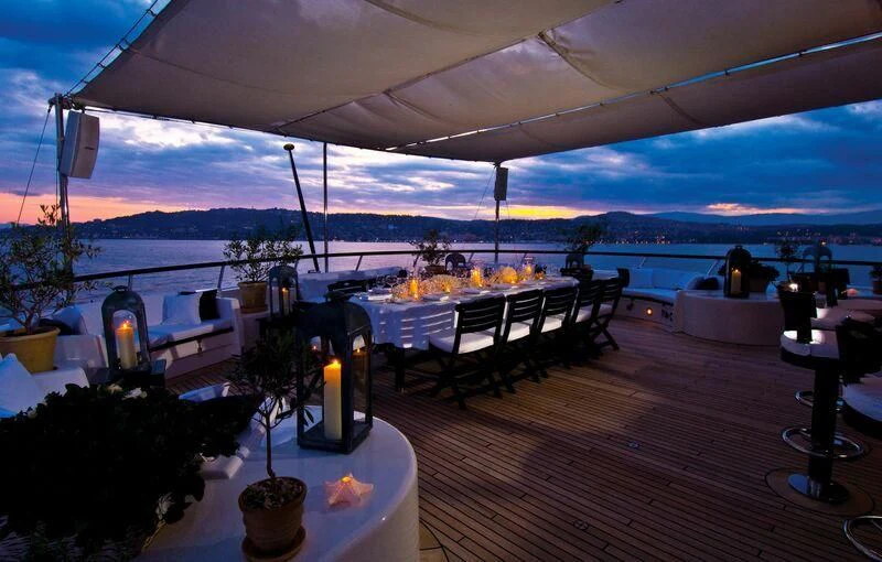 a table with a bottle of wine on a patio with a view of the ocean and a city aboard VIRGINIAN Yacht for Sale