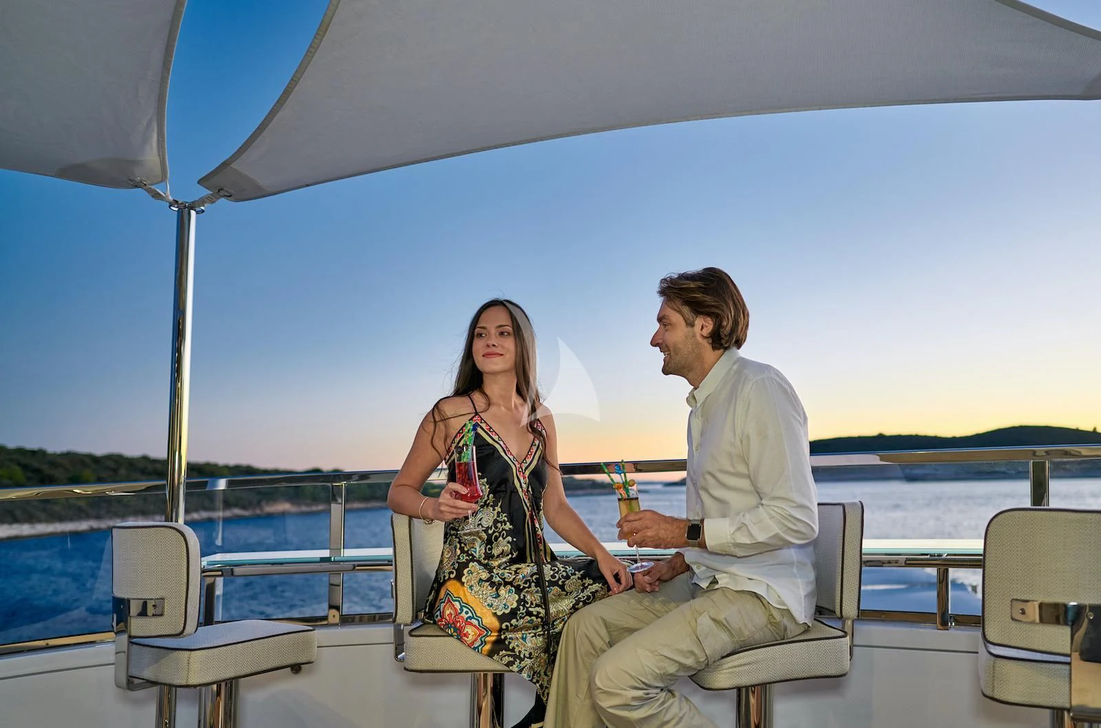 a man and woman sitting on a boat with a drink and a glass of wine aboard HAPPY ME Yacht for Charter