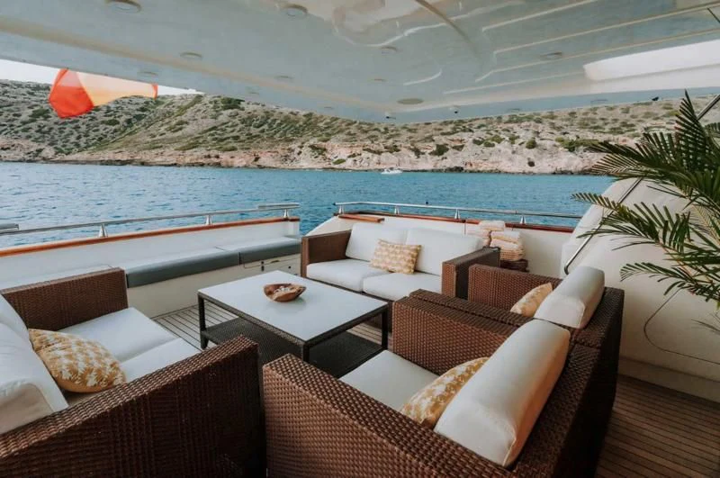 a room with a couch and a table and chairs with a body of water in the background aboard SONRISA SEPTIMO Yacht for Sale